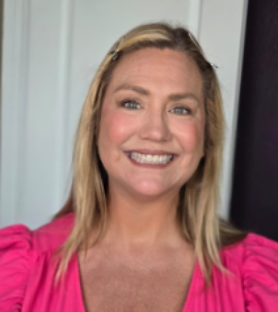 A smiling woman over 40 with blonde hair and natural makeup wearing a bright pink top, showcasing a fresh and confident look.
