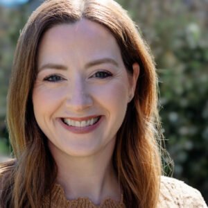 A smiling woman over 40 with natural makeup and long brown hair, showcasing radiant beauty outdoors.