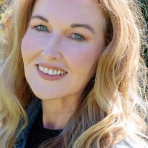 A smiling woman over 50 with radiant satin skin, natural pro-aging makeup, and blonde wavy hair, showcasing a healthy glow.