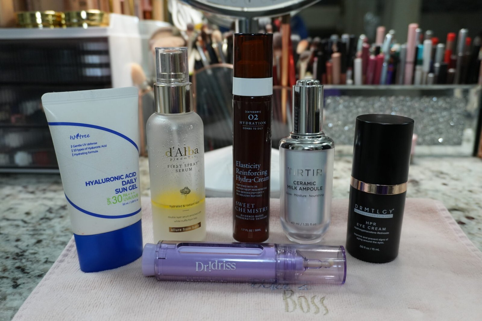 A lineup of hydrating skincare products for menopausal skin, including Tirtir Milk Ampoule, Dr. Idriss Major Fade, and D'Alba Serum Spray on a bathroom vanity.