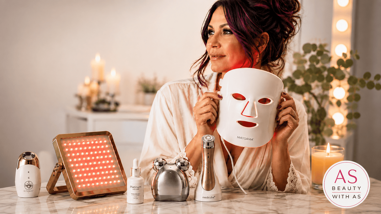 Beauty tech devices over 50, including a woman holding an LED light therapy mask beside skincare tools on a marble vanity.
